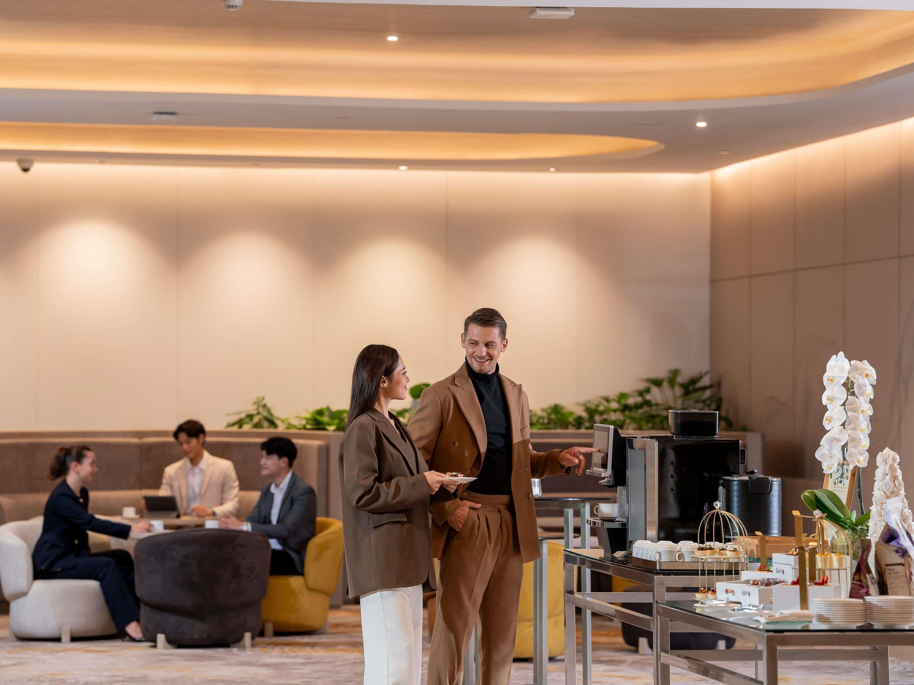 A modern hotel lobby with a seating area, a buffet table with various food items, and a coffee station.