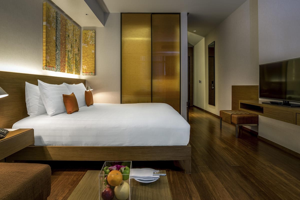 Una habitación de hotel moderna con una cama grande, un televisor, una mesita de noche de madera y una mesilla con una lámpara.