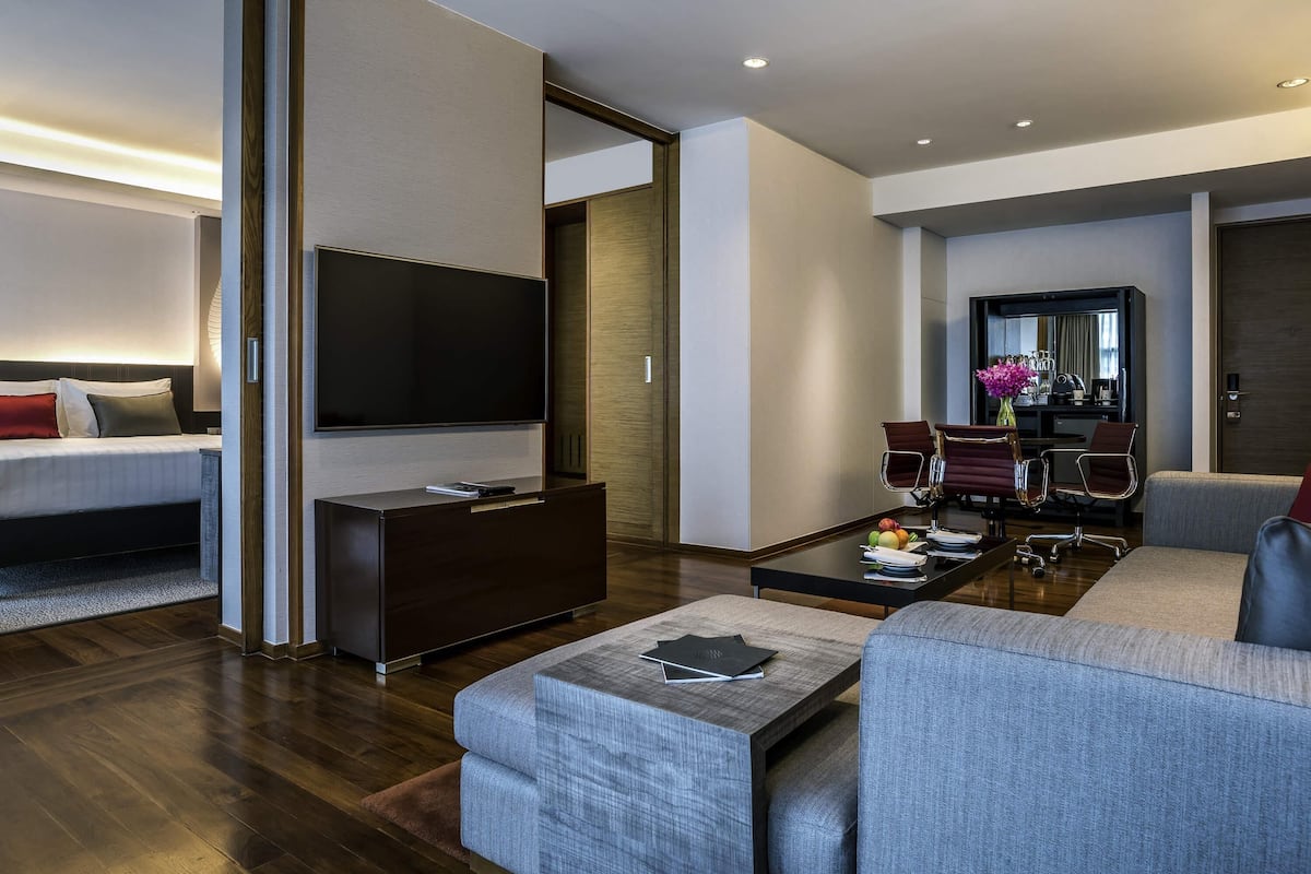 Una habitación de hotel moderna con una cama, un televisor, un sofá, una mesa de centro y un comedor con sillas y una mesa.