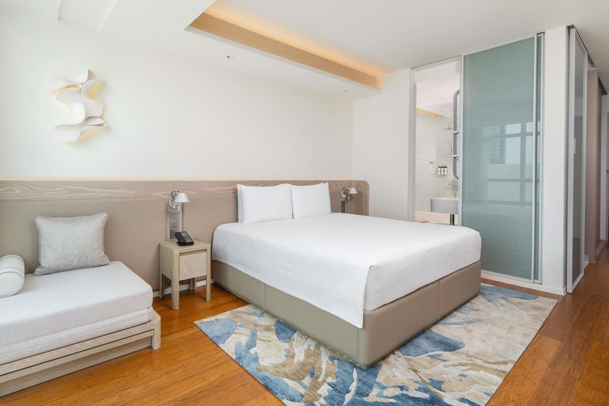 Una habitación de hotel moderna con cama, mesita de noche, lámpara y sofá.