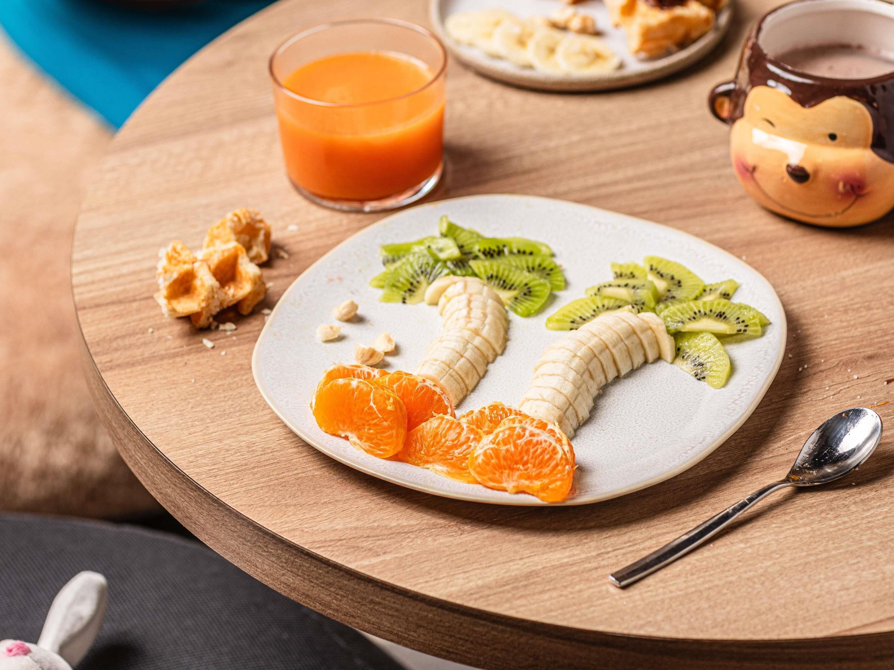 A breakfast plate with fruit, a glass of orange juice, and a ceramic mug on a wooden table.