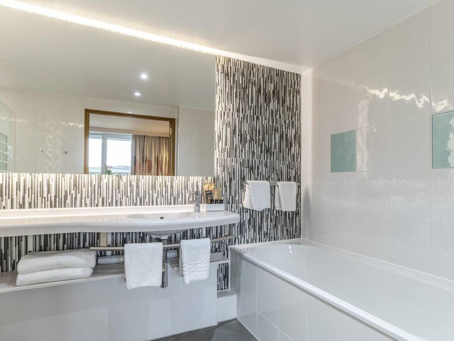 A modern bathroom with a large mirror, two sinks, a bathtub, and a striped wall design.