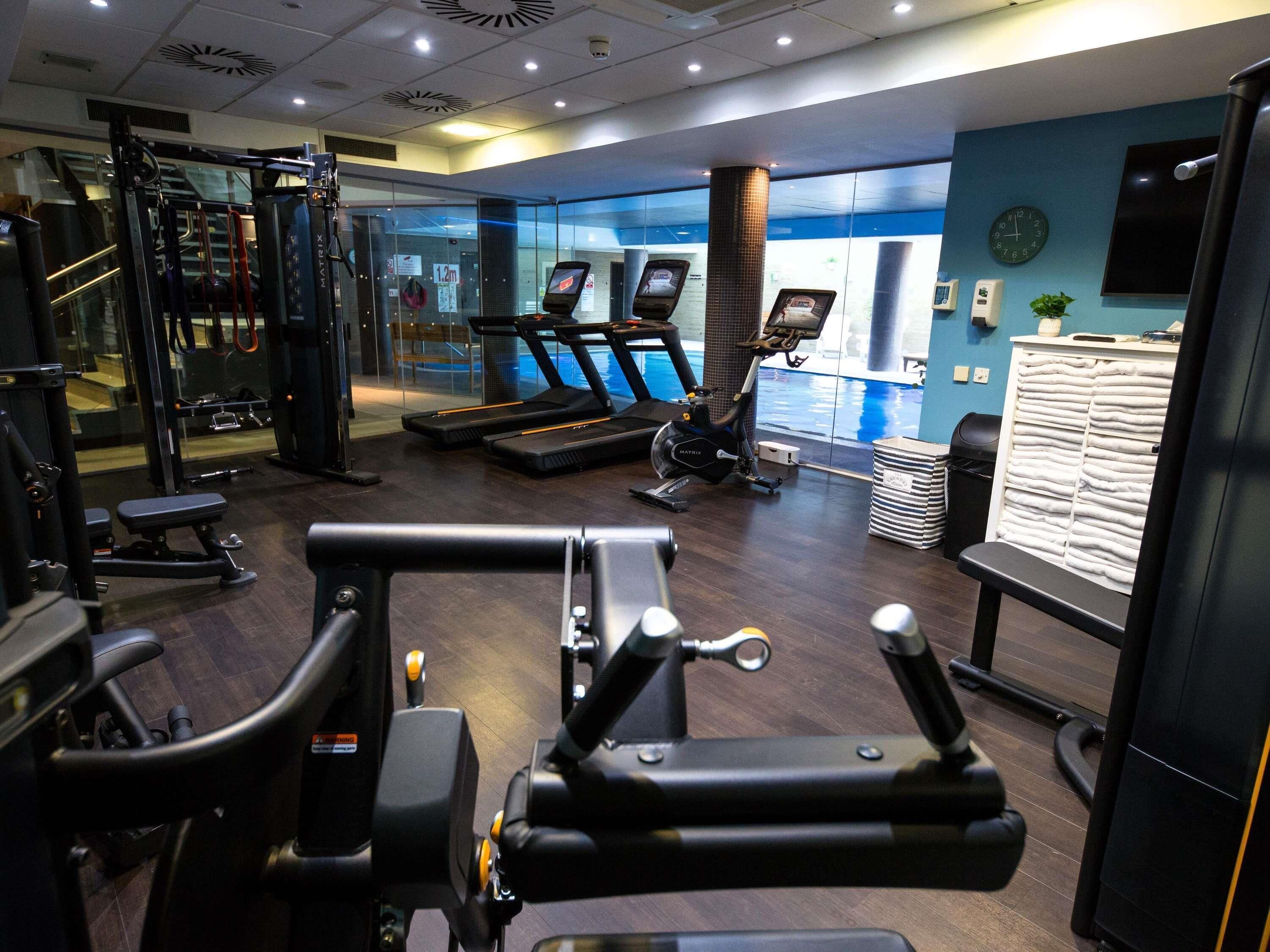 A gym with treadmills, weight machines, and a pool visible through the glass wall.