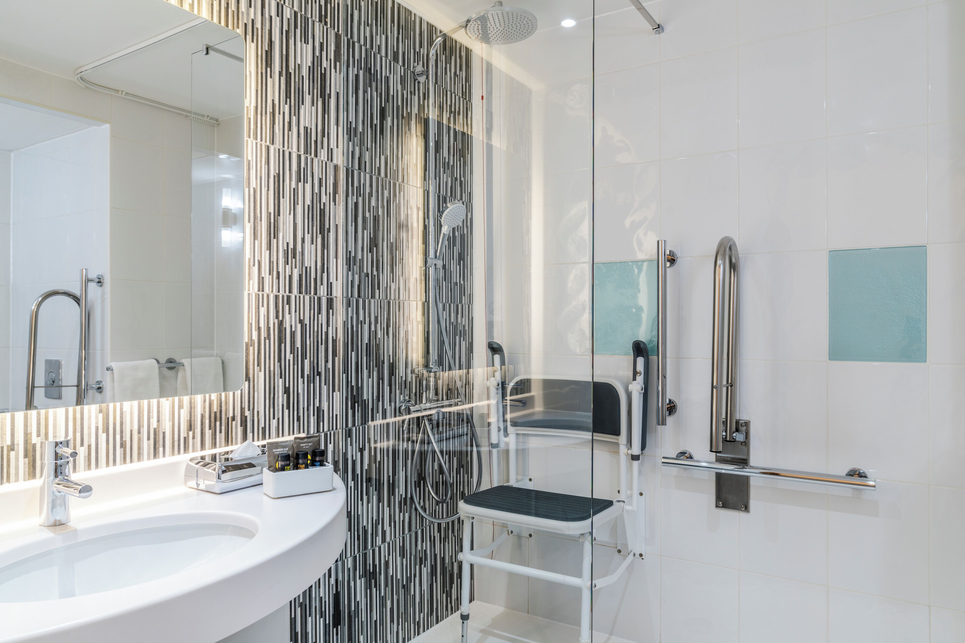 A modern bathroom with a large mirror, two sinks, a shower with a handheld showerhead, and a glass partition.