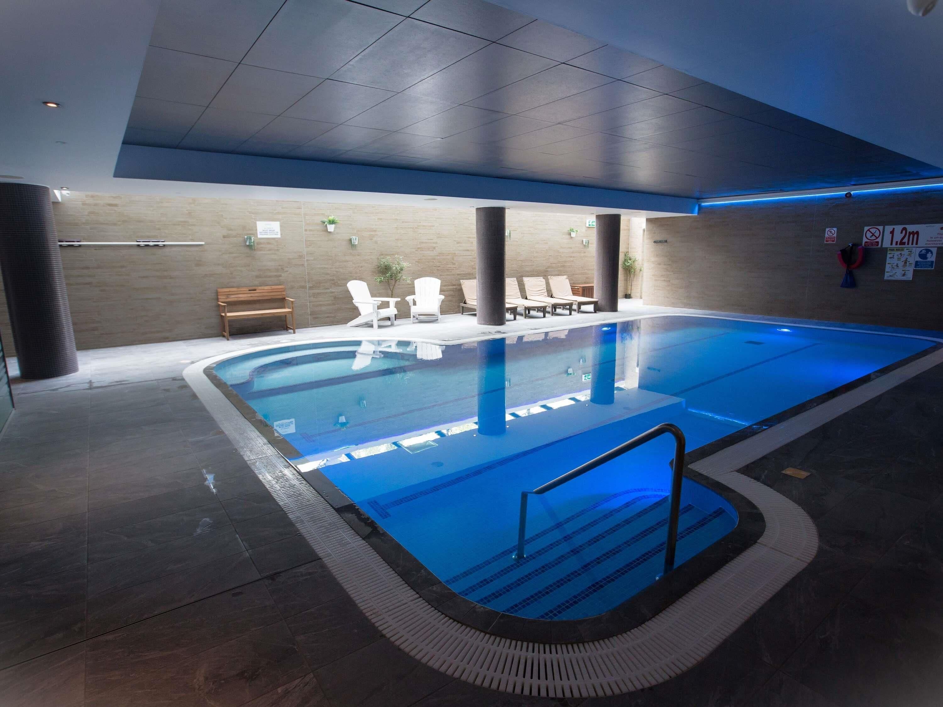 Une piscine intérieure avec des lignes de démarcation bien visibles, des chaises longues et un banc en bois.
