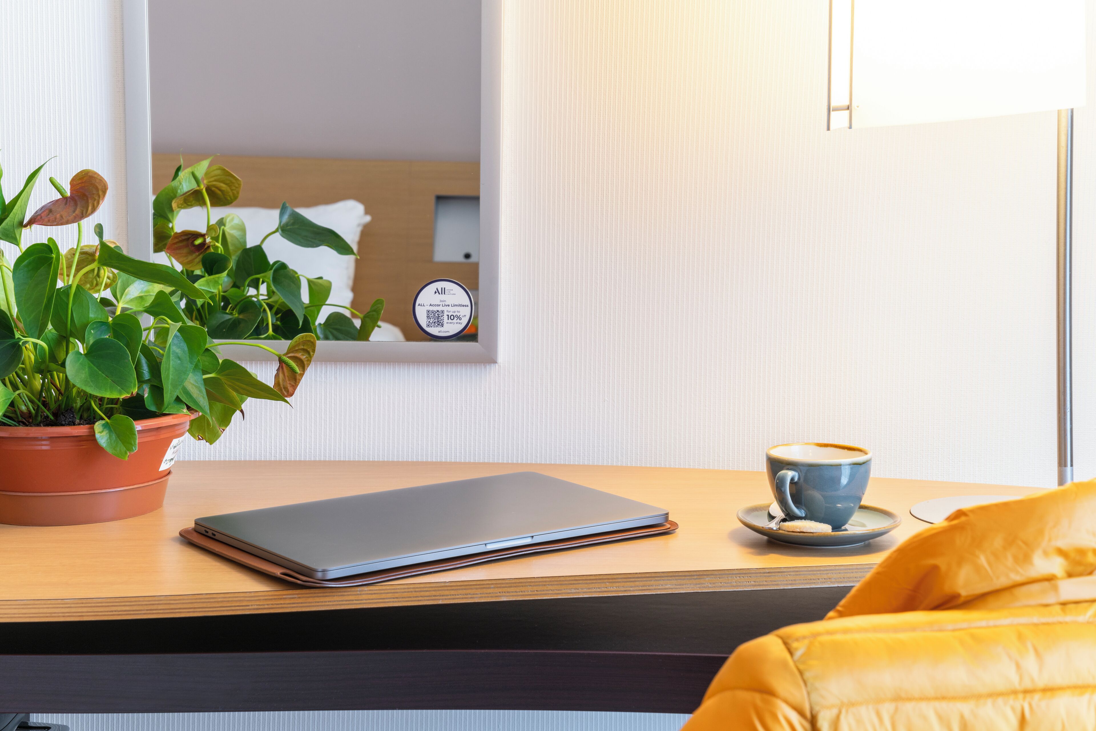 A laptop on a wooden table, a potted plant, and a cup of coffee.