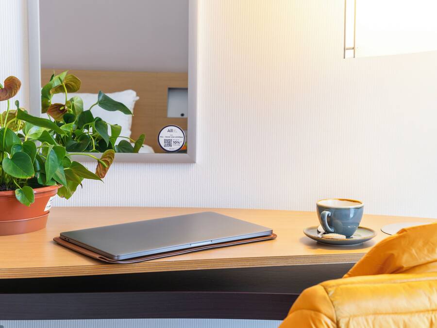 Een laptop op een houten tafel, een potplant en een koffiekop.