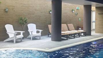 Zona junto a la piscina con sillones de descanso, una mesita y una planta en maceta.