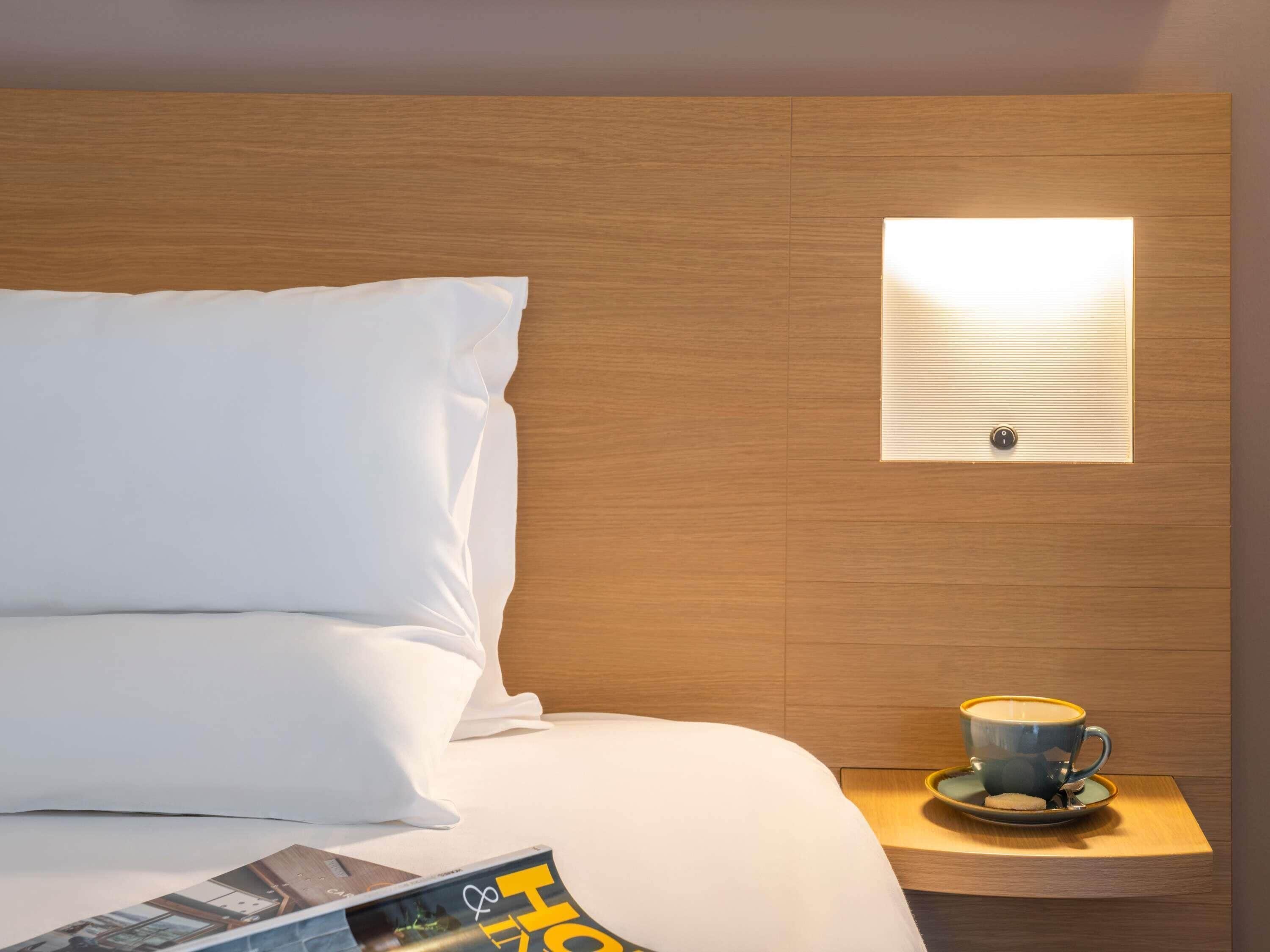 A hotel room with a bed, a nightstand, a lamp, and a magazine.