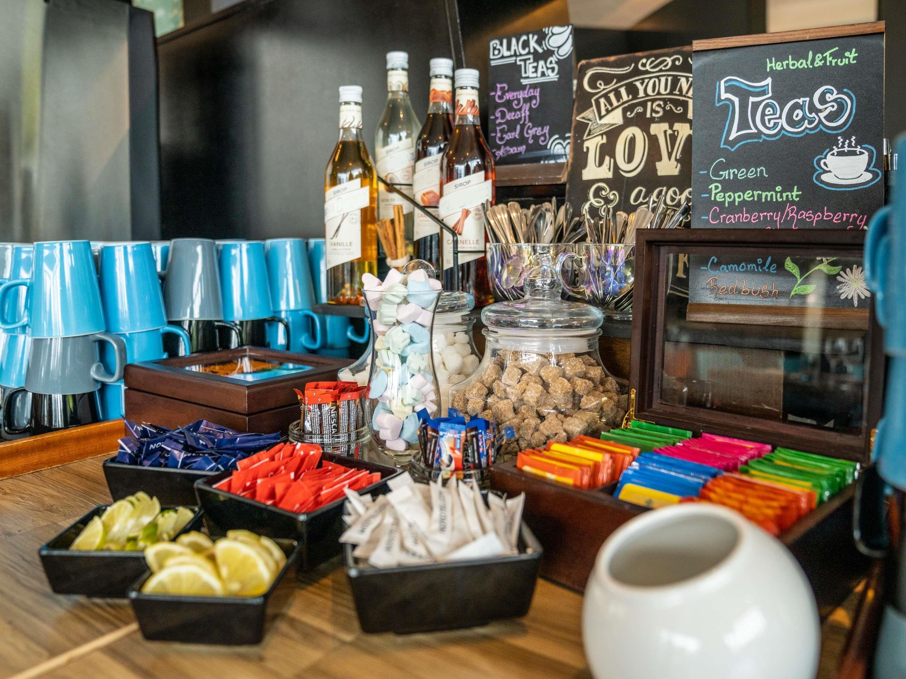 A coffee station with various tea options, a chalkboard menu, and a selection of snacks.