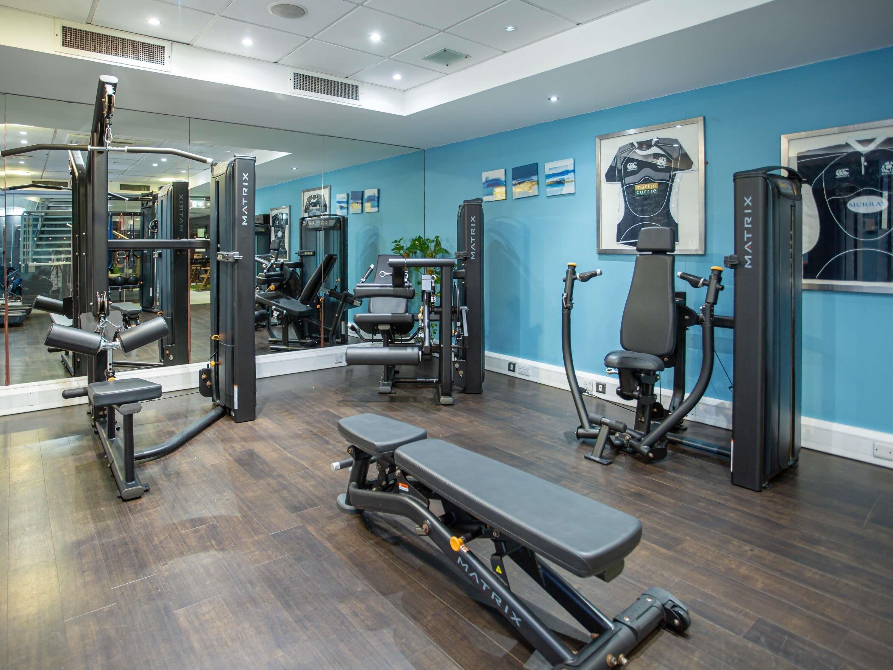 Un gimnasio con paredes espejadas, equipamiento de ejercicio y una banca.