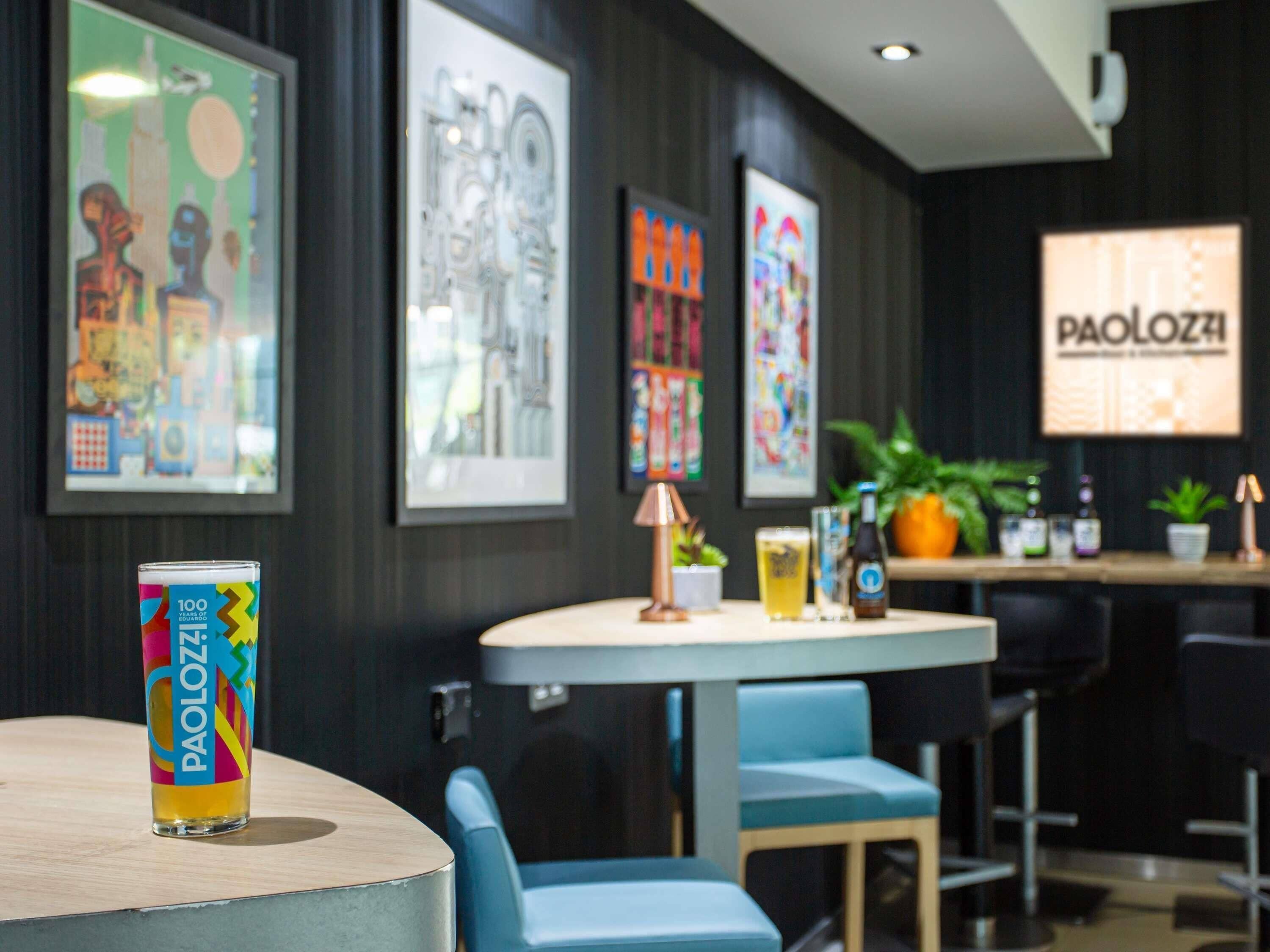 A bar area with a round table, blue chairs, and a framed sign reading 'PAOLOZZI'.