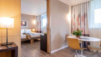 Ein Hotelzimmer mit Bett, Nachttisch, Lampe, Stuhl und einem Tisch mit Pflanze.