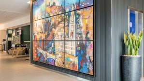 Eine moderne Lobby mit einem großen, abstrakten Stadtbild, einer Rezeption und einem Topf mit Pflanze.