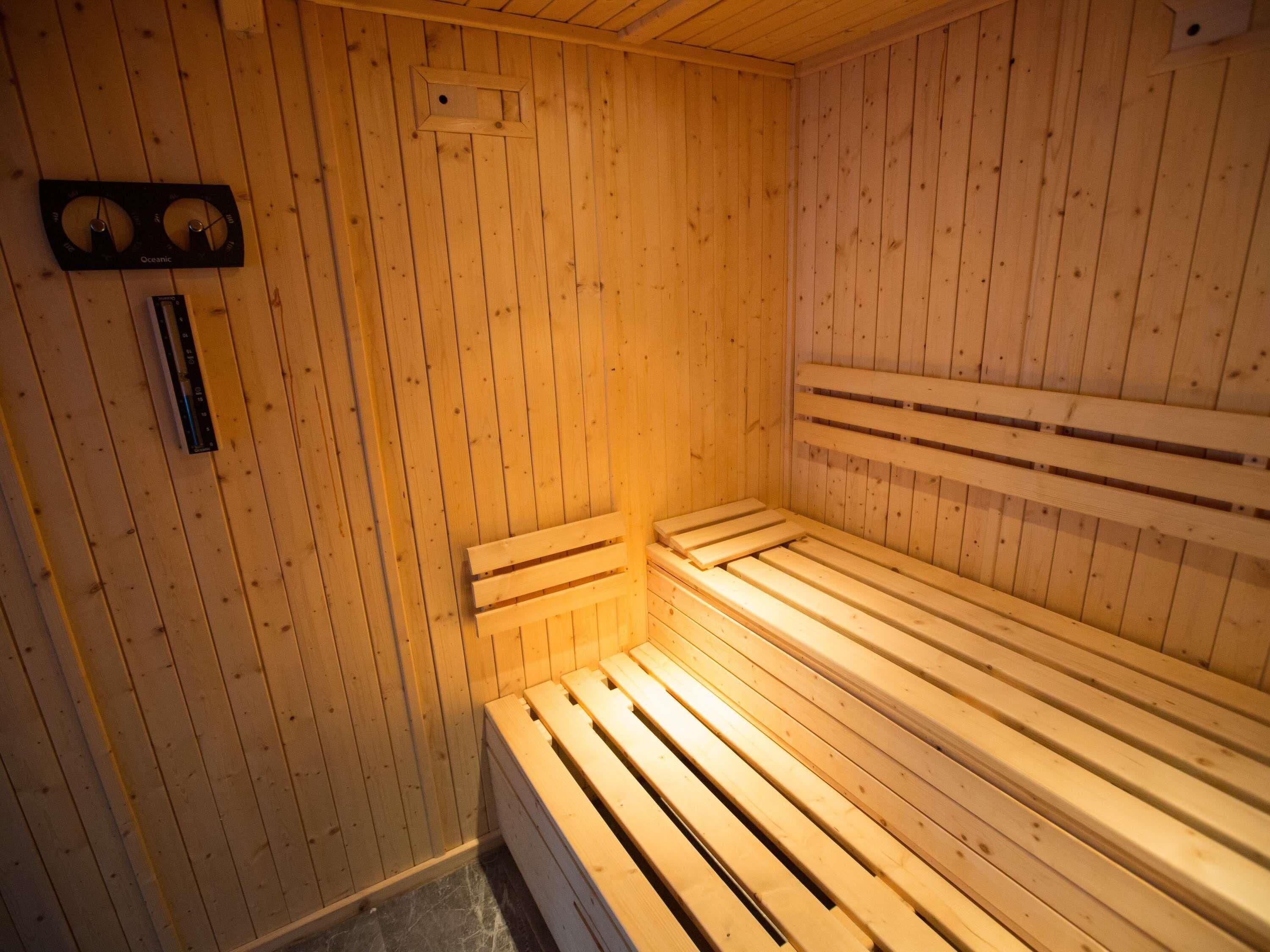 A sauna room with wooden benches and a wall-mounted control panel.