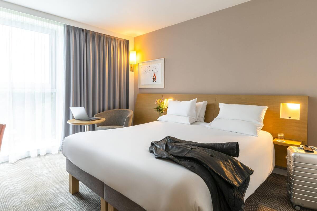 Habitación de hotel con una cama grande, un escritorio, una silla, una maleta y una ventana con cortinas.