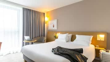 A hotel room with a large bed, a desk, a chair, a suitcase, and a window with curtains.