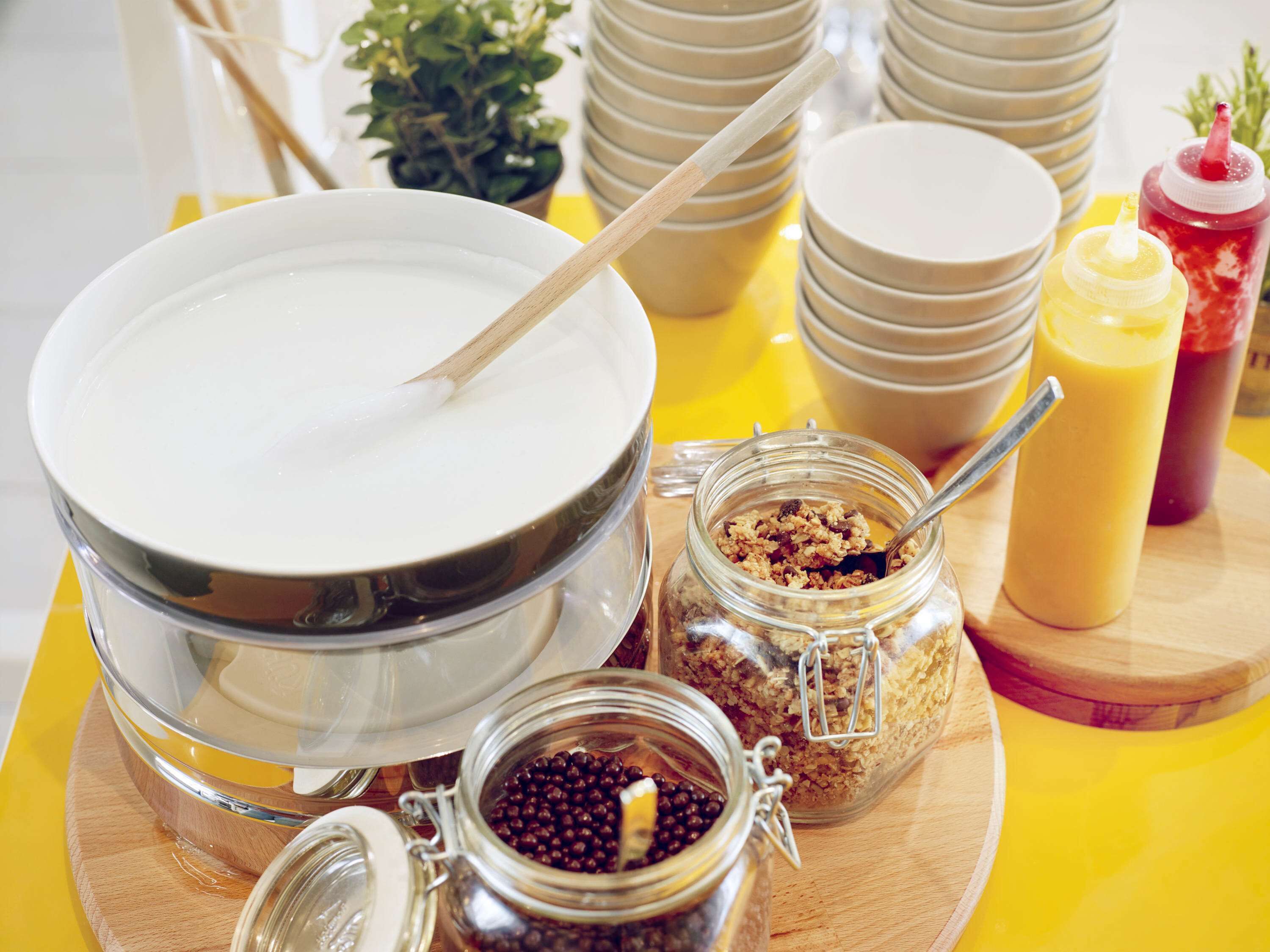 A breakfast setup with a bowl of cereal, a jar of berries, and condiments on a wooden board.