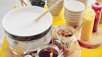 A breakfast setup with a bowl of cereal, a jar of berries, and condiments on a wooden board.