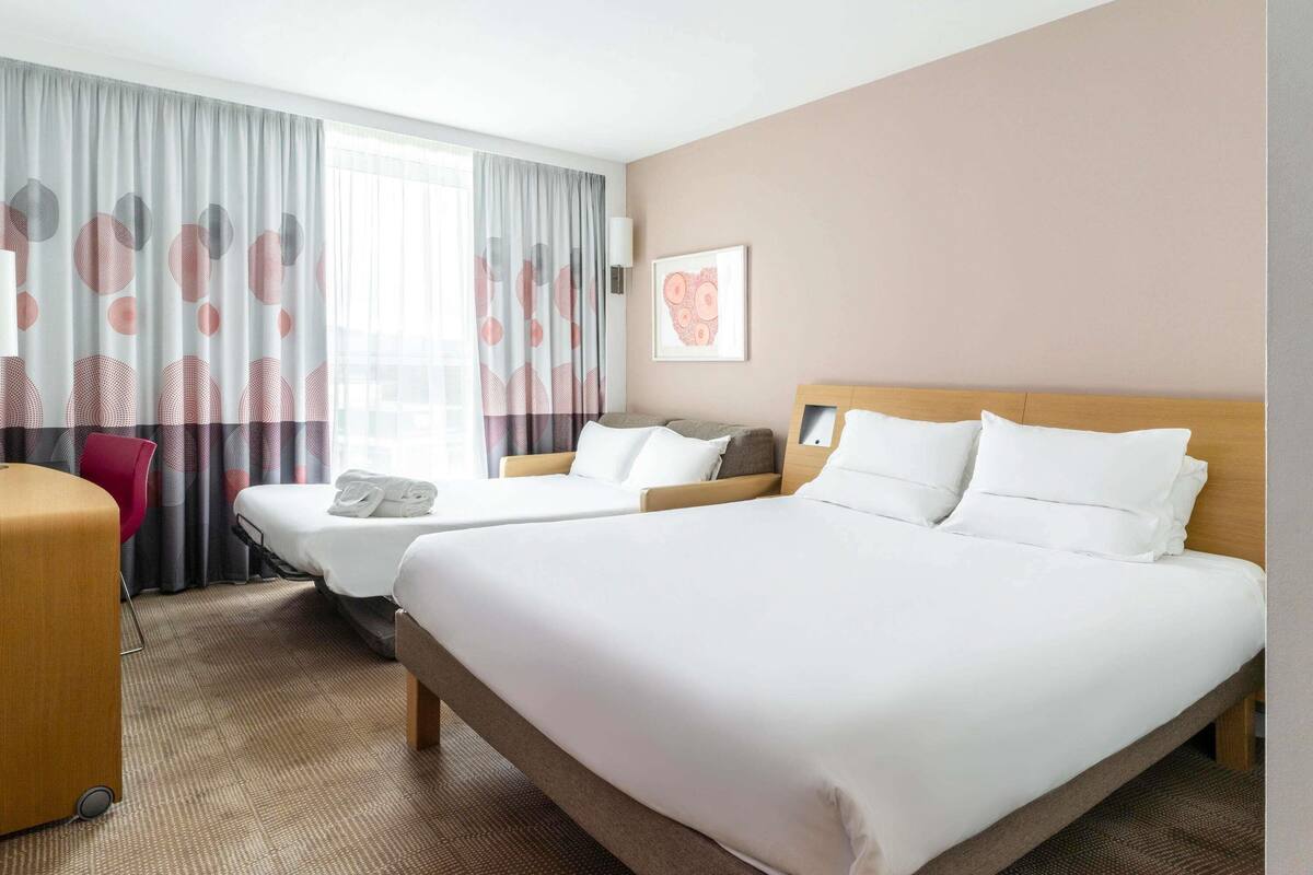 A hotel room with two beds, a desk, and a chair.