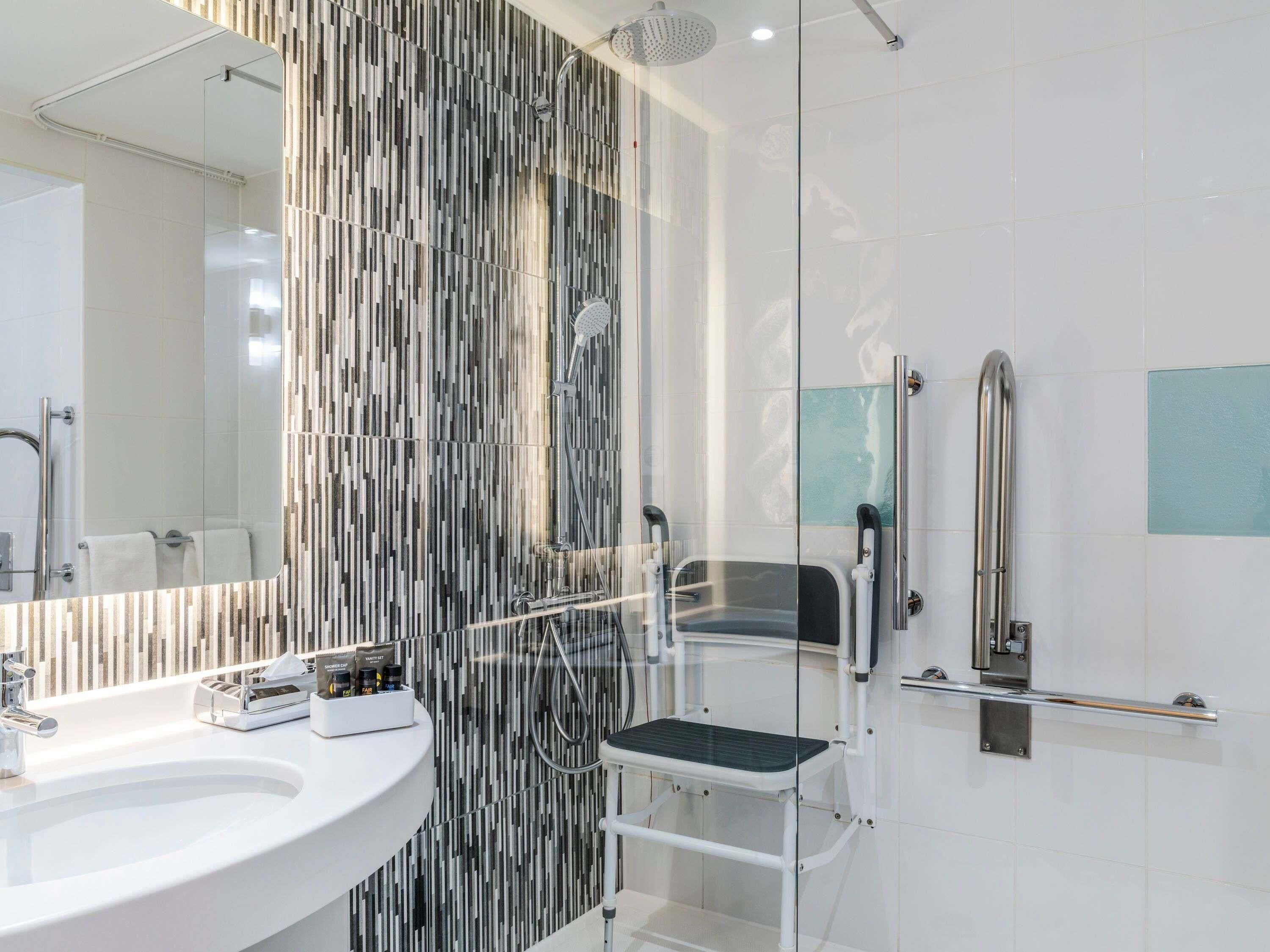 A modern bathroom with a glass shower enclosure, a white sink, and a step stool.
