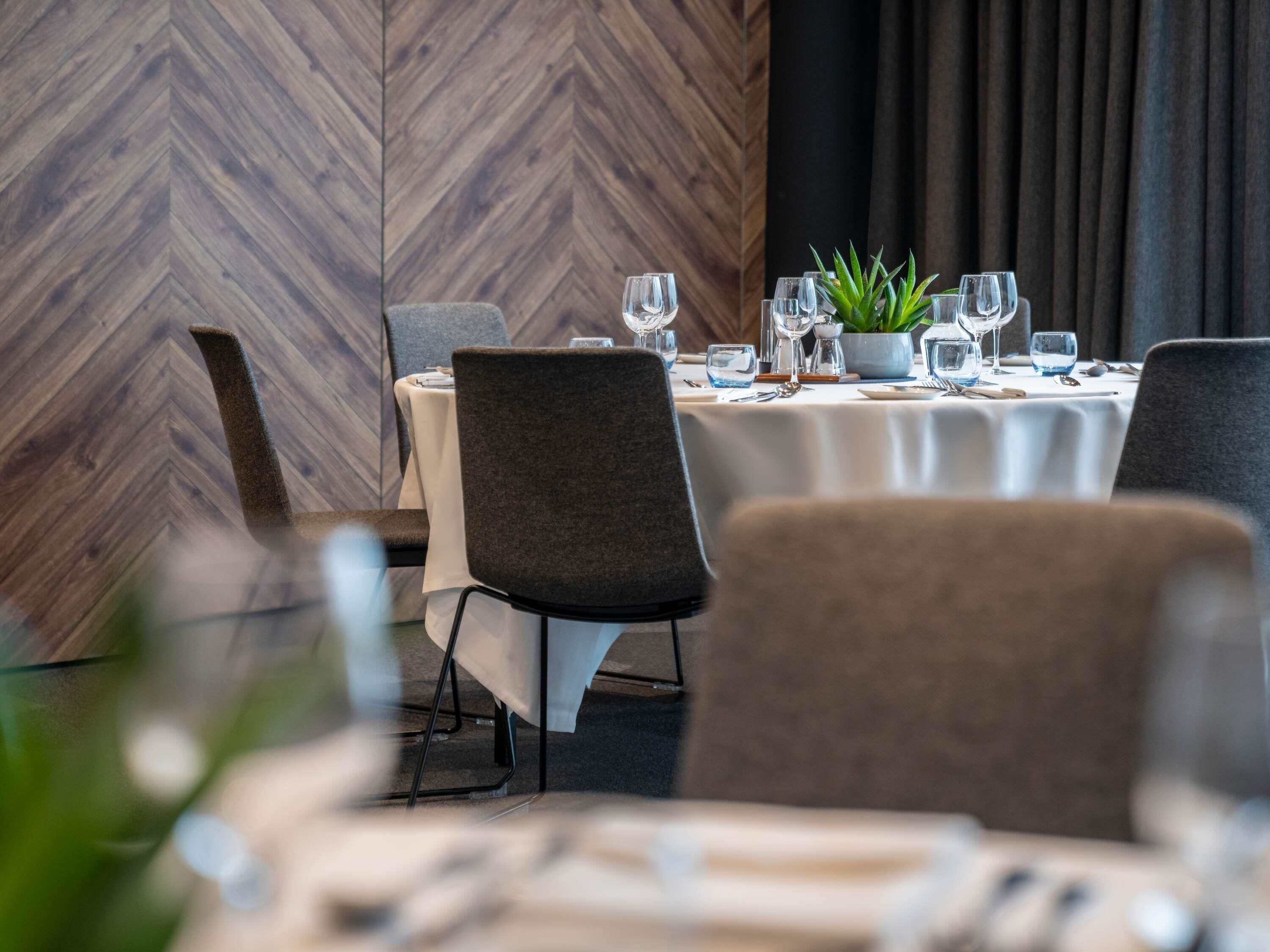 A dining area with a herringbone wood wall, round tables with chairs, and a potted plant.
