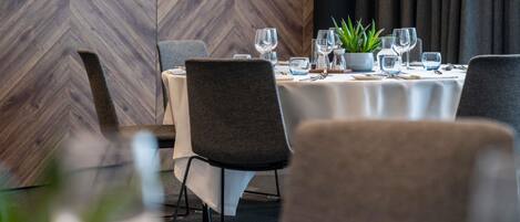 A dining area with a herringbone wood wall, round tables with chairs, and a potted plant.
