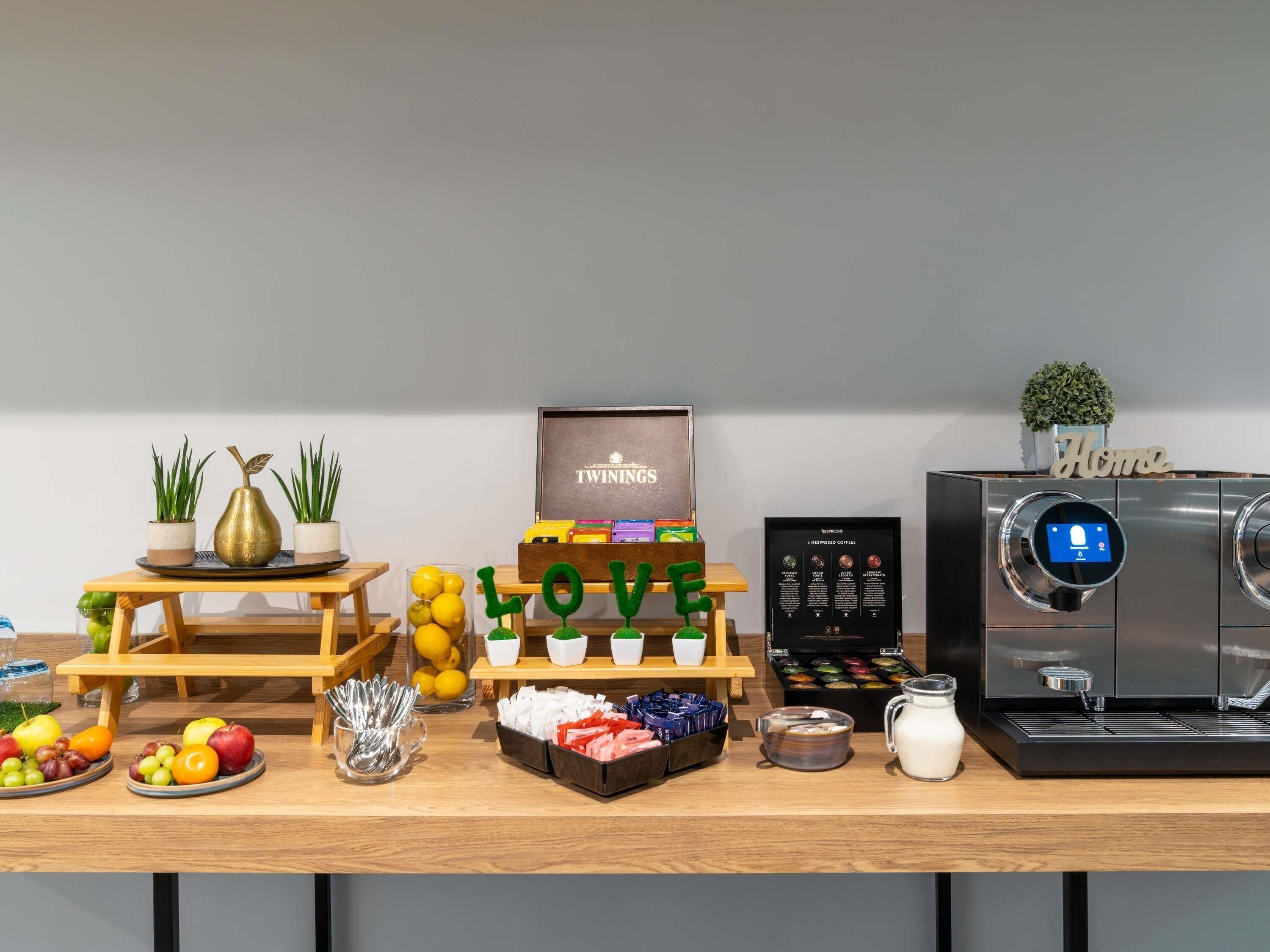 Een koffiehoek met een koffieapparaat, een bord waarop 'TWININGS' staat, en een presentatie van koffiecups.