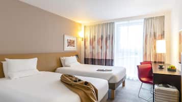 Habitación de hotel con dos camas, un escritorio, una silla, una lámpara y una maleta.