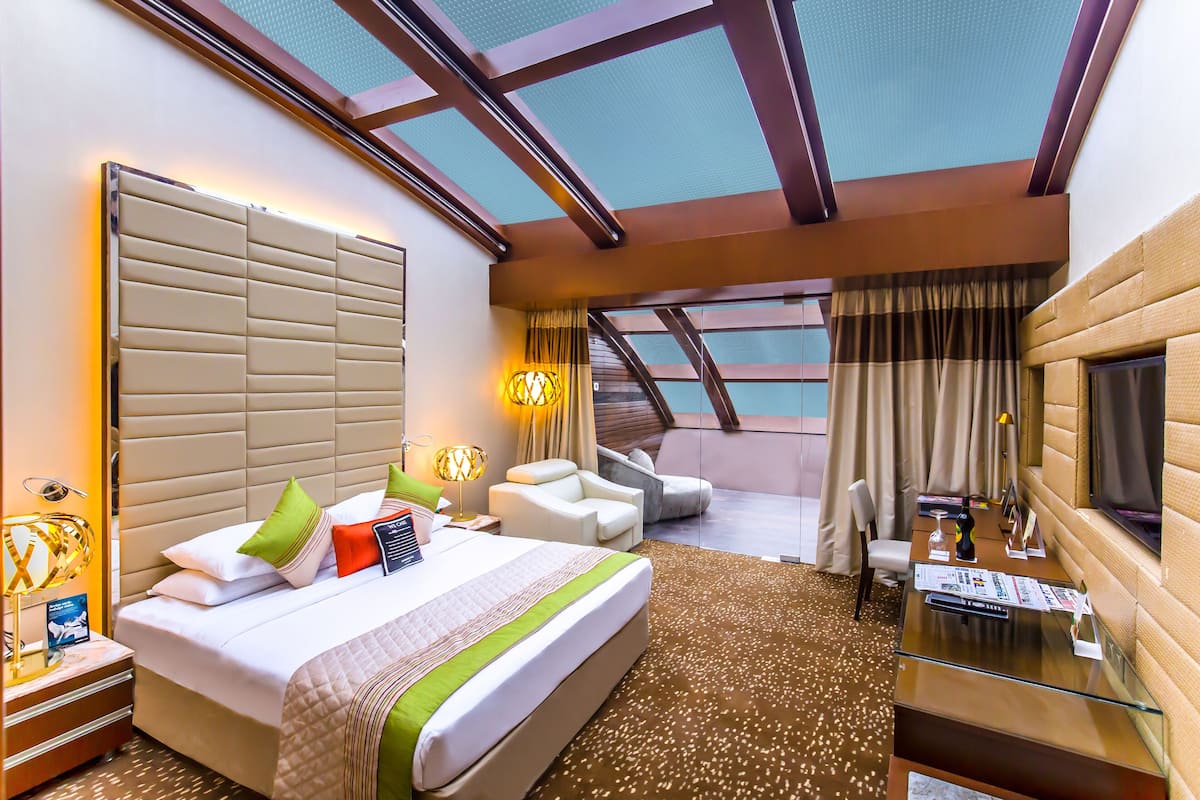 Une chambre d’hôtel avec un grand lit, un bureau, une chaise, une télévision et un balcon avec des rideaux.
