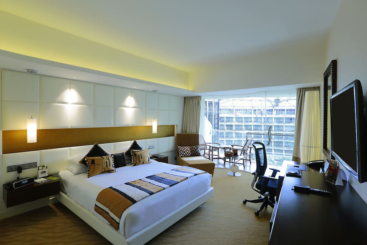 Une chambre d’hôtel avec un grand lit, un bureau avec un ordinateur, une télévision et un balcon offrant une vue sur un navire de croisière.