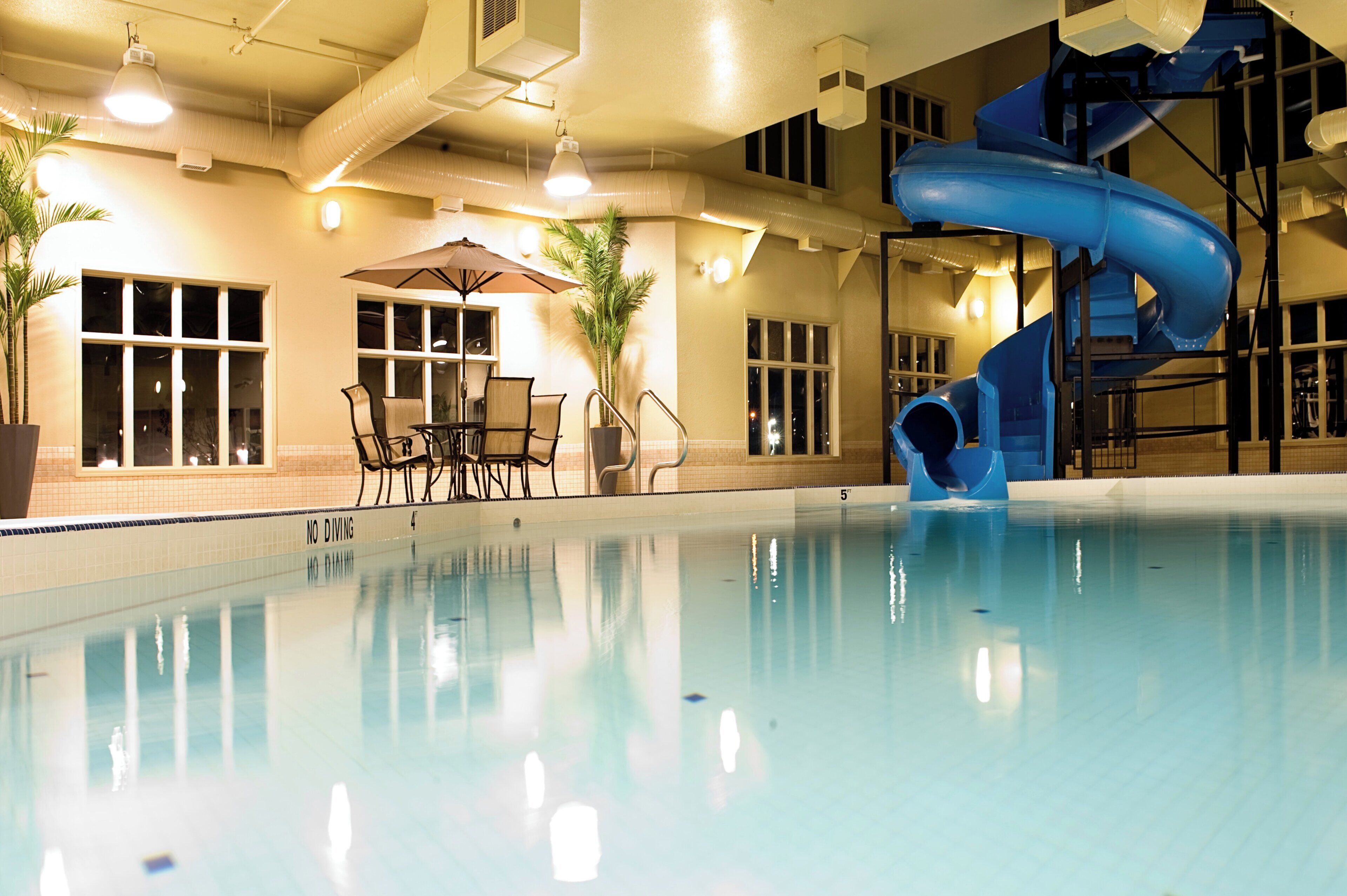Una piscina al coperto con uno scivolo blu, area relax e piante in vaso.