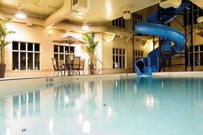 An indoor swimming pool with a blue slide, seating area, and potted plants.