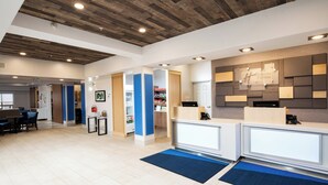 A hotel reception area with a wooden ceiling, a reception desk, a blue carpet, and a wall-mounted sign. - Holiday Inn Express & Suites Grande Prairie by IHG (Grande Prairie)