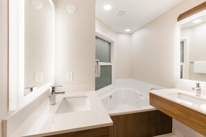 Un baño moderno con una bañera grande, dos lavamanos y un mueble de tocador de madera.