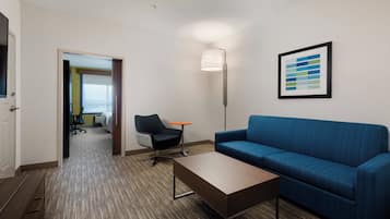 Ein Hotelzimmer mit einem blauen Sofa, einem Holztisch, einem modernen Sessel, einer Stehlampe und einem gerahmten abstrakten Kunstwerk an der Wand.