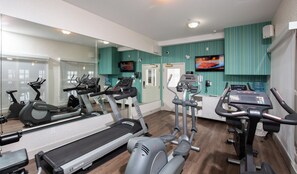 A gym with various exercise equipment, a large mirror, and a television on the wall.