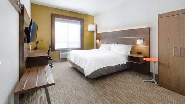 Habitación de hotel con cama, escritorio, silla, televisión, lámpara y armario.