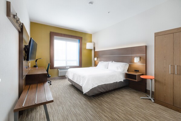Habitación de hotel con cama, escritorio, silla, televisión, lámpara y armario.