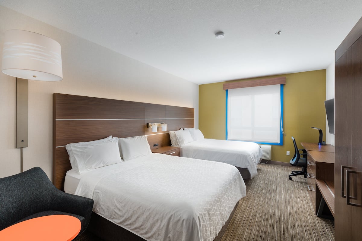 A hotel room with two beds, a desk, a chair, and a lamp.