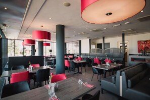 A modern restaurant interior with high ceilings, red and black chairs, and tables set for dining. - Bastion Hotel Rotterdam Alexander (Rotterdam)