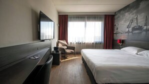 Een hotelkamer met een bed, een bureau, een stoel, een televisie en een groot raam met gordijnen.