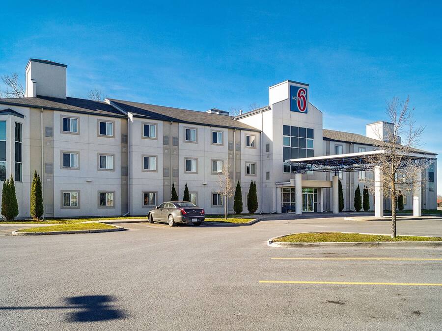 Un hôtel moderne doté d’un grand parking, d’une entrée couverte et d’un logo « 6 » bien visible sur le bâtiment.