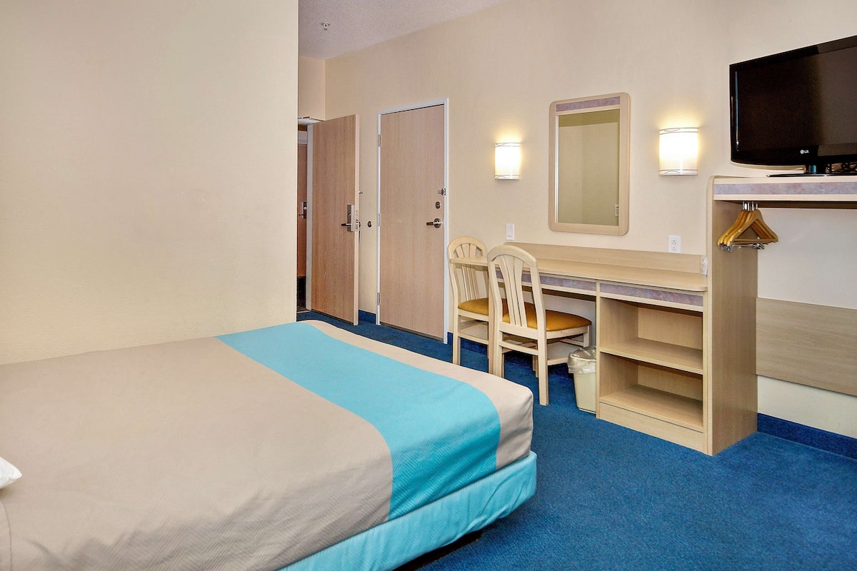 Ein Hotelzimmer mit Bett, Schreibtisch, Stuhl, Fernseher und Spiegel.