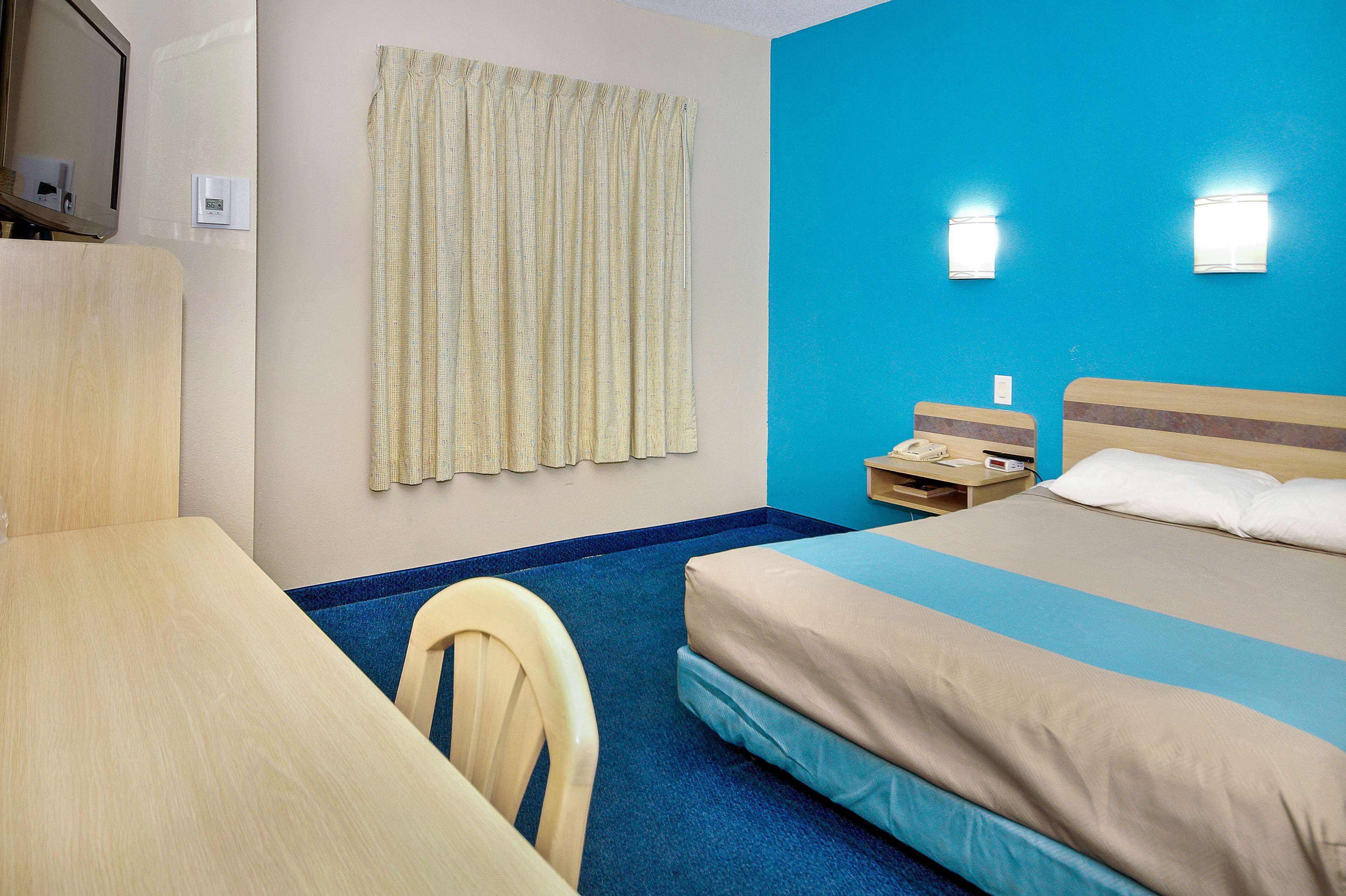 Une chambre d’hôtel équipée d’un lit, d’un bureau, d’une chaise, d’un rideau et d’un téléphone fixé au mur.