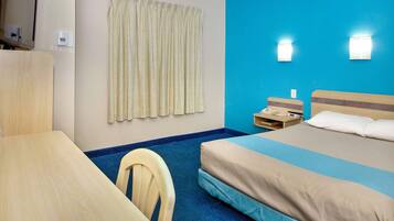 Habitación de hotel con cama, escritorio, silla, cortina y teléfono instalado en la pared.