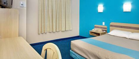 Camera d'albergo con un letto, una scrivania, una sedia, una tenda e un telefono fissato al muro.