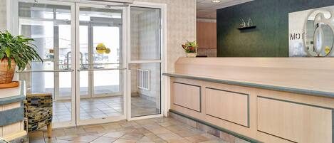 A hotel reception area with a glass door entrance, a reception desk, and a potted plant.
