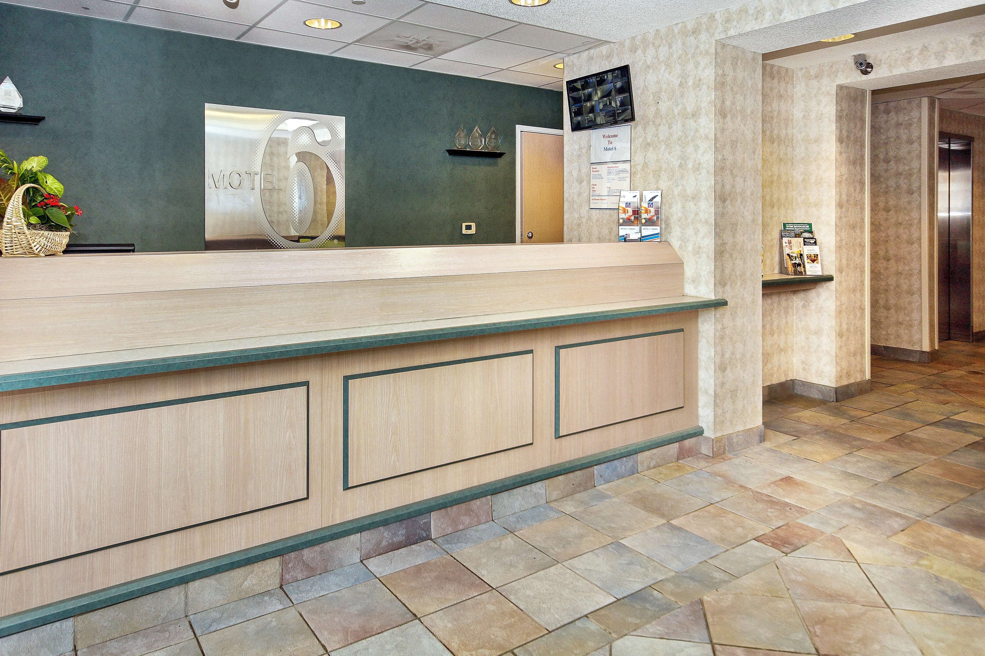 A hotel reception desk with a 'Motel 6' sign, a reception area, and a tiled floor.