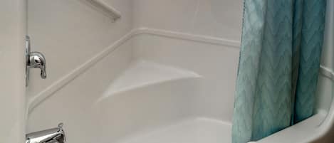 Une baignoire avec un mur recouvert de carreaux blancs, un robinet chromé et une serviette blanche.